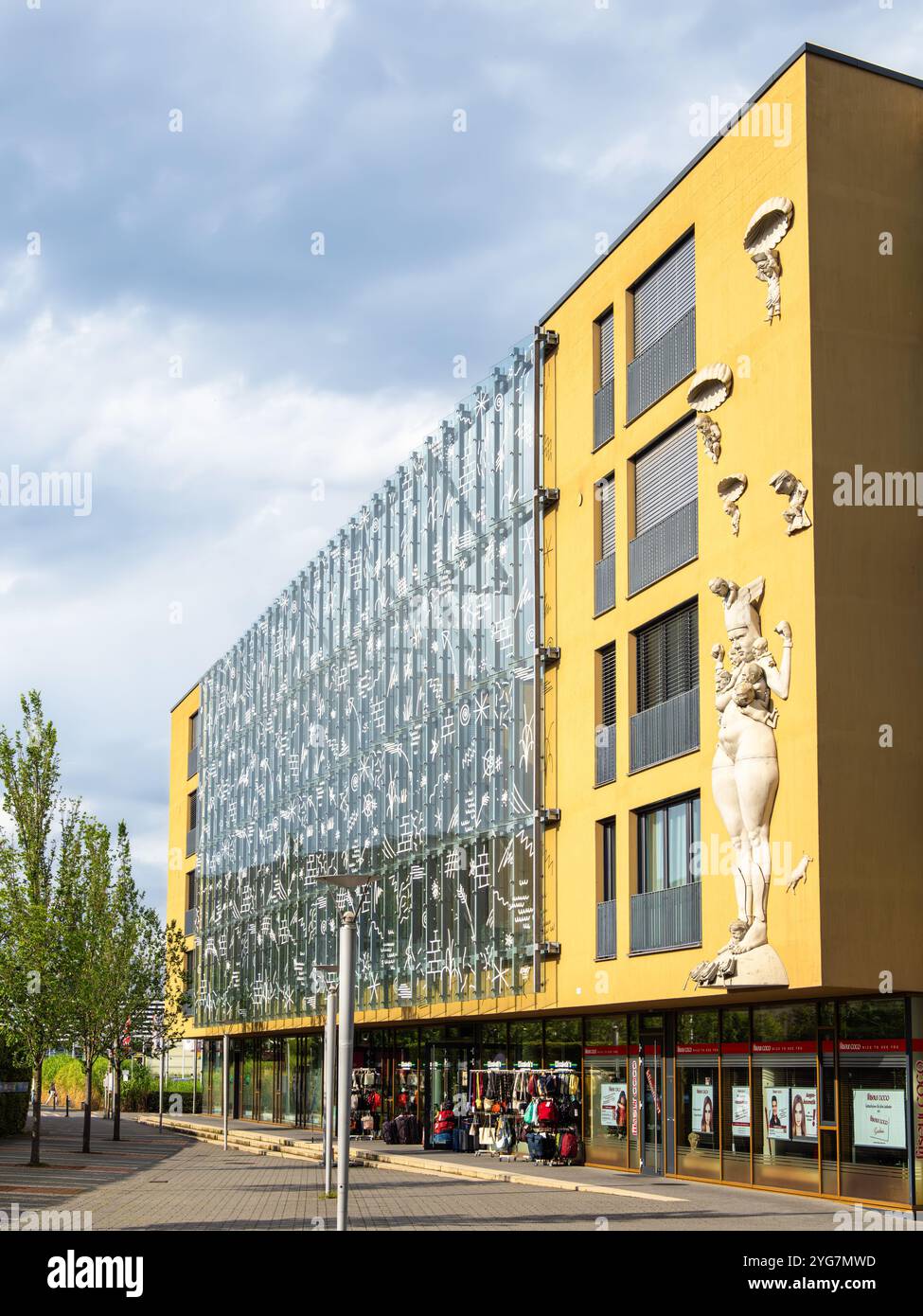 Radolfzell, Germania - 2 agosto 2024: Un moderno edificio giallo con una facciata in vetro con elementi artistici e sculture. Foto Stock