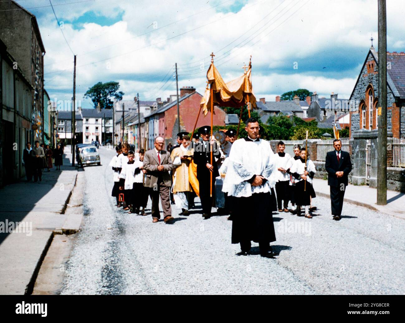 Un sacerdote guida la festa dei colori della processione del Corpus Christi a Castleisland, Contea di Kerry, Irlanda. I membri del Garda Siochana portano lo striscione. Foto Stock