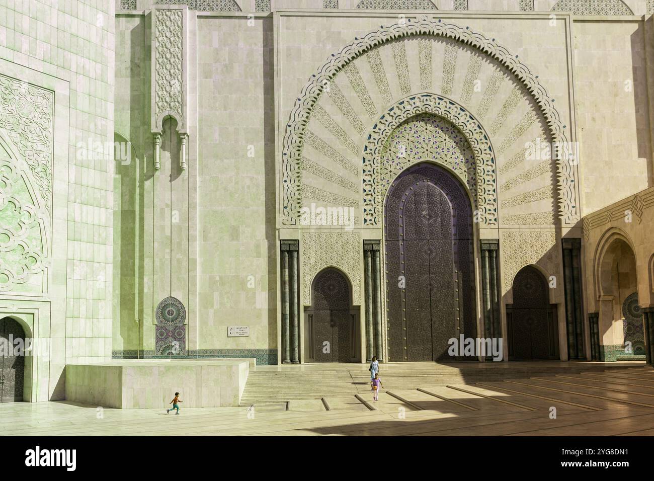Madre, figlia e figlio giocano vicino alle imponenti mura della Moschea Hassan II a Casablanca, in Marocco, mostrando la splendida architettura della moschea Foto Stock