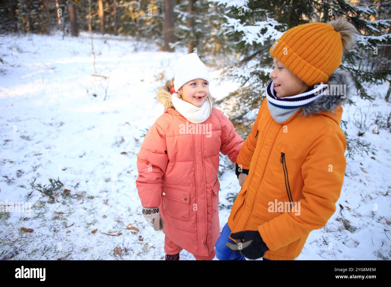 Un fratello e una sorella camminano insieme gioiosamente attraverso una tranquilla foresta innevata, circondata da alti alberi ricoperti di bianco. Foto Stock