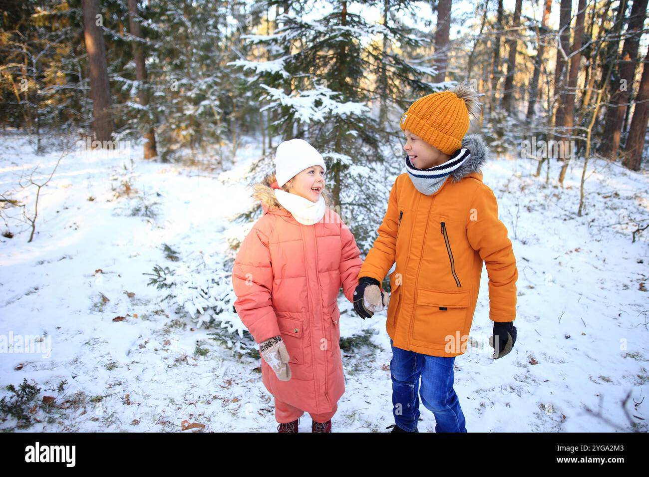 Un fratello e una sorella camminano insieme gioiosamente attraverso una tranquilla foresta innevata, circondata da alti alberi ricoperti di bianco. Foto Stock