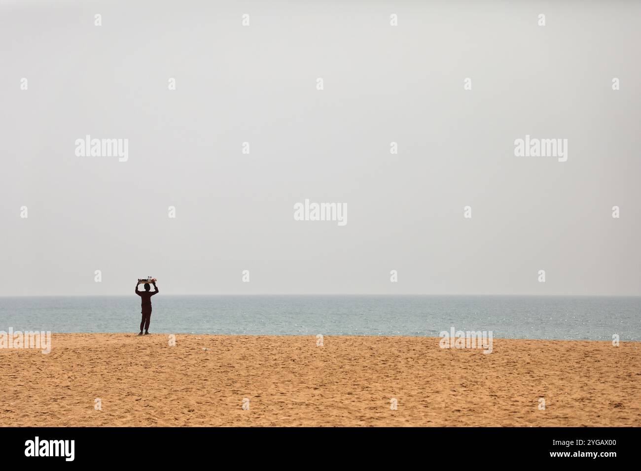 Ouidah, Benin. 10 gennaio 2022. Di fronte allo spazio assegnato al festival voodoo di Ouidah, Benin, un giovane venditore ambulante cammina lungo la spiaggia su e giù. Ogni 10 gennaio, a Ouidah, Benin, si tiene una festa voodoo per celebrare le divinità di questa religione dell'Africa occidentale, vicino alla porta del non ritorno, che commemora la deportazione di milioni di prigionieri durante il commercio degli schiavi. Nata nel Benin, la religione Vodun o Voodoo deriva da tradizioni animiste, e si basa sul legame con la natura e gli antenati. (Foto di Apolline Guillerot-Malick/SOPA Images/Sipa USA) credito: SIPA USA/Alamy Live News Foto Stock