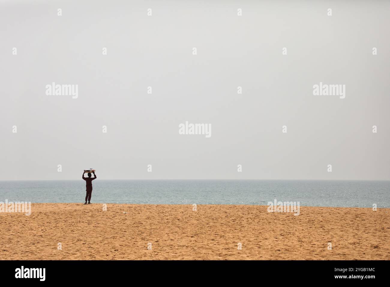 Ouidah, Atlantica, Benin. 10 gennaio 2022. Di fronte allo spazio assegnato al festival voodoo di Ouidah, Benin, un giovane venditore ambulante cammina lungo la spiaggia su e giù. Ogni 10 gennaio, a Ouidah, Benin, si tiene una festa voodoo per celebrare le divinità di questa religione dell'Africa occidentale, vicino alla porta del non ritorno, che commemora la deportazione di milioni di prigionieri durante il commercio degli schiavi. Nata nel Benin, la religione Vodun o Voodoo deriva da tradizioni animiste, e si basa sul legame con la natura e gli antenati. (Immagine di credito: © Apolline Guillerot-Malick/SOPA Images via ZUMA Press Wire) EDI Foto Stock