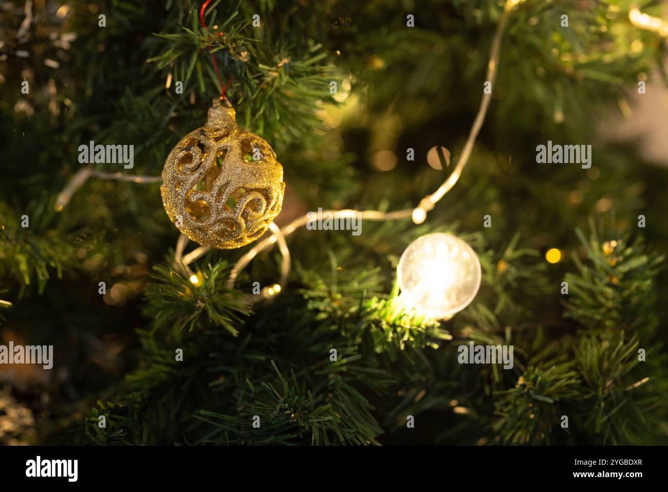 Appendere un ornamento dorato sull'albero di Natale con luci accese che creano un'atmosfera festosa a casa Foto Stock