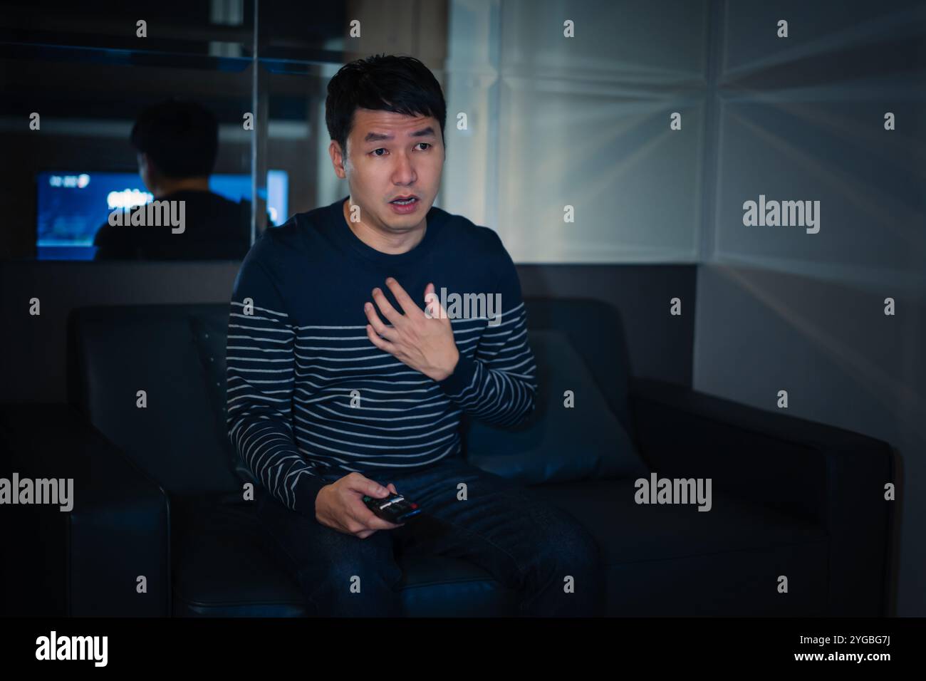 L'uomo scioccato sta guardando la TV sul divano di notte Foto Stock