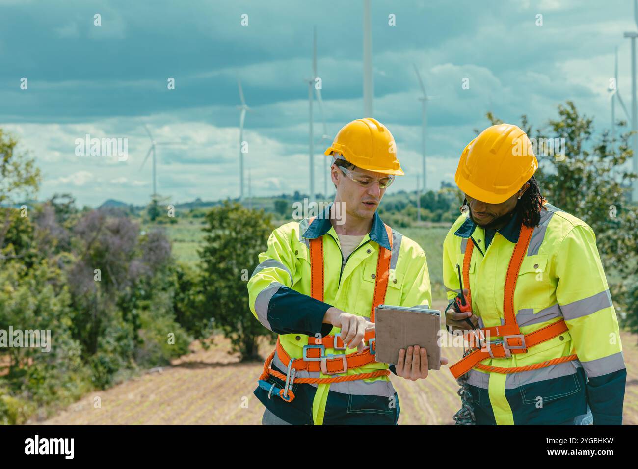 I tecnici che utilizzano un servizio di computer tablet monitorano lo stato di Wind Turbines, lavorando a un'indagine presso un campo di produzione di energia eolica all'aperto. Foto Stock I tecnici che utilizzano un servizio di computer tablet monitorano lo stato di Wind Turbines, lavorando a un'indagine presso un campo di produzione di energia eolica all'aperto. Foto Stock