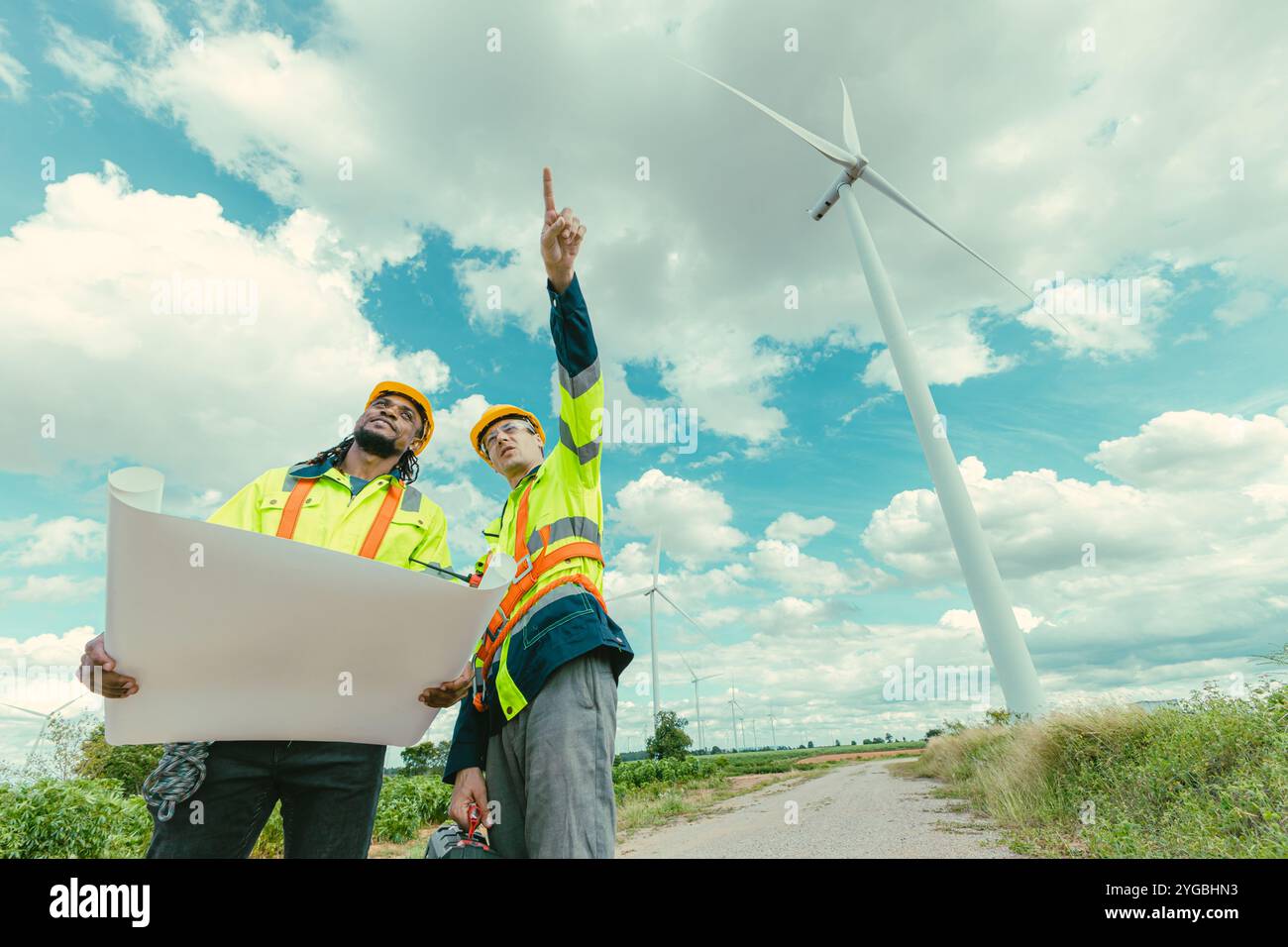 Il team di ingegneri mescola lavoratori maschi in bianco e nero con la planimetria del sondaggio sul lavoro sul campo di Wind Turbines presso il campo agricolo di generatori di energia eolica all'aperto. Foto Stock Il team di ingegneri mescola lavoratori maschi in bianco e nero con la planimetria del sondaggio sul lavoro sul campo di Wind Turbines presso il campo agricolo di generatori di energia eolica all'aperto. Foto Stock