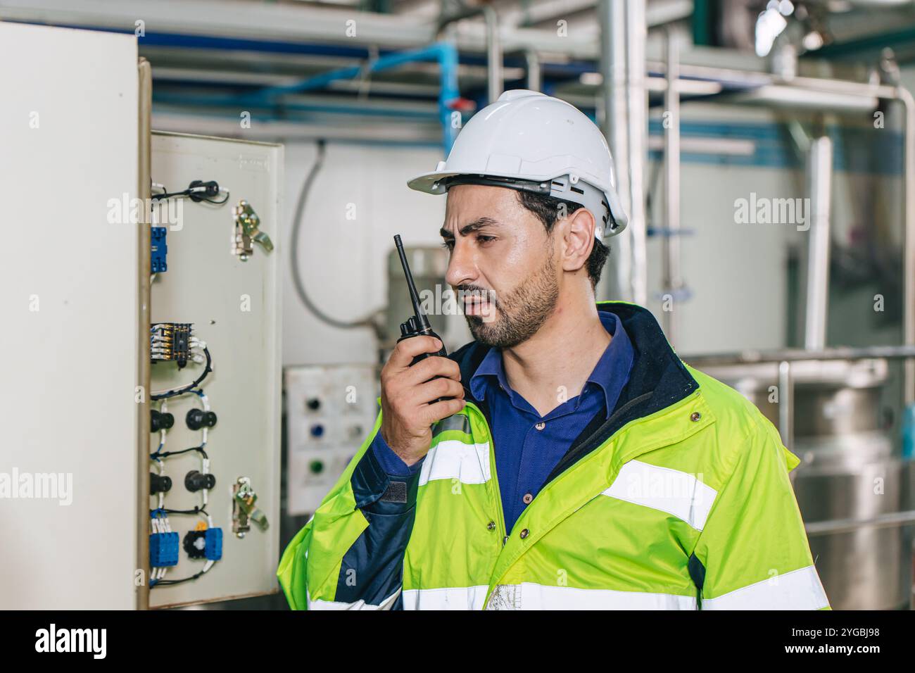 Ingegnere in servizio, lavoratore latino maschio in fabbrica in una centrale elettrica a gas e petrolio con controllo, gestisce l'ordine con comunicazione walkie-talkie al lavoro Foto Stock
