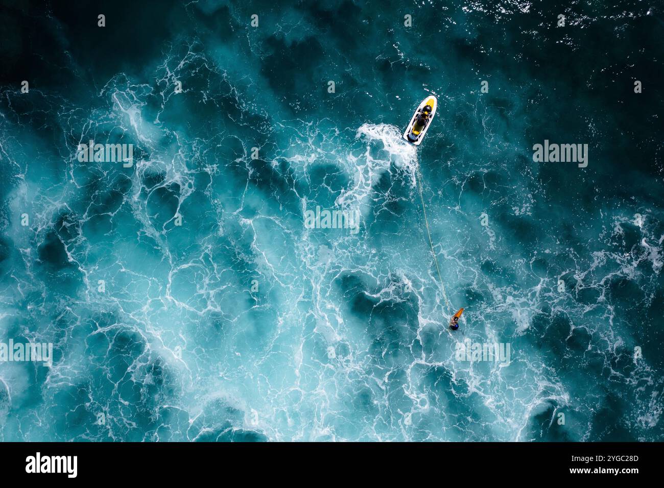 Moto d'acqua e surfista in azione, surf trainato in mezzo al mare blu profondo con acqua torbida, schiuma marina e spruzzi. Drone aereo sparato da una vista dall'alto Foto Stock