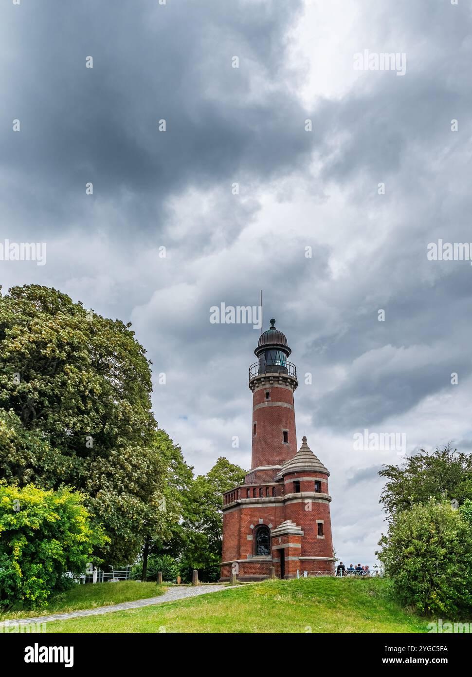 Un suggestivo faro in mattoni adagiato su un cielo coperto e' circondato da lussureggianti frontoni verdi, creando un'atmosfera drammatica e storica. Questo tranqui Foto Stock