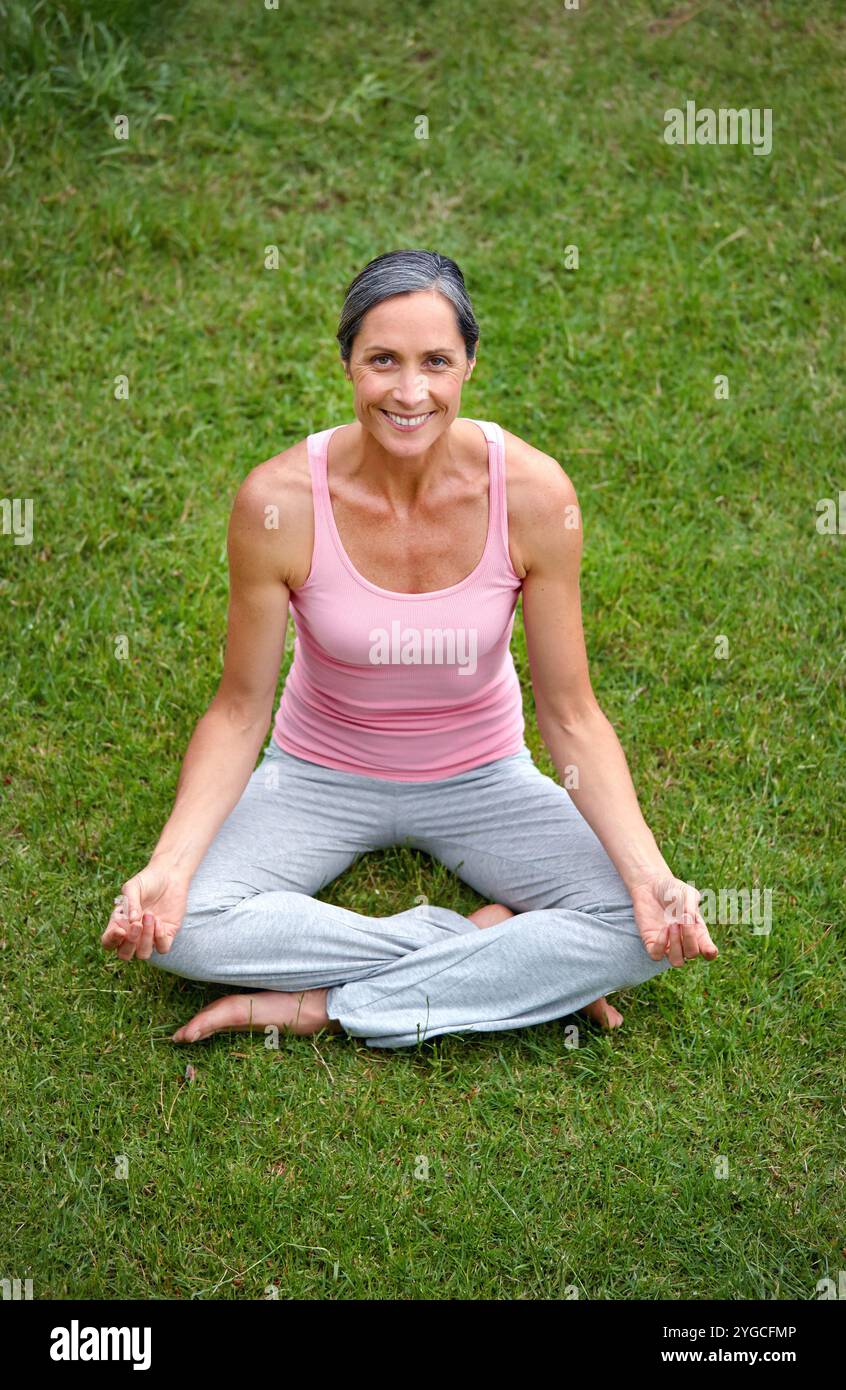 Donna felice, all'aperto e loto in yoga per ritratti, meditazione o pace in giardino. Persona fisica matura, zen e sorridi sull'erba per lo spirito Foto Stock