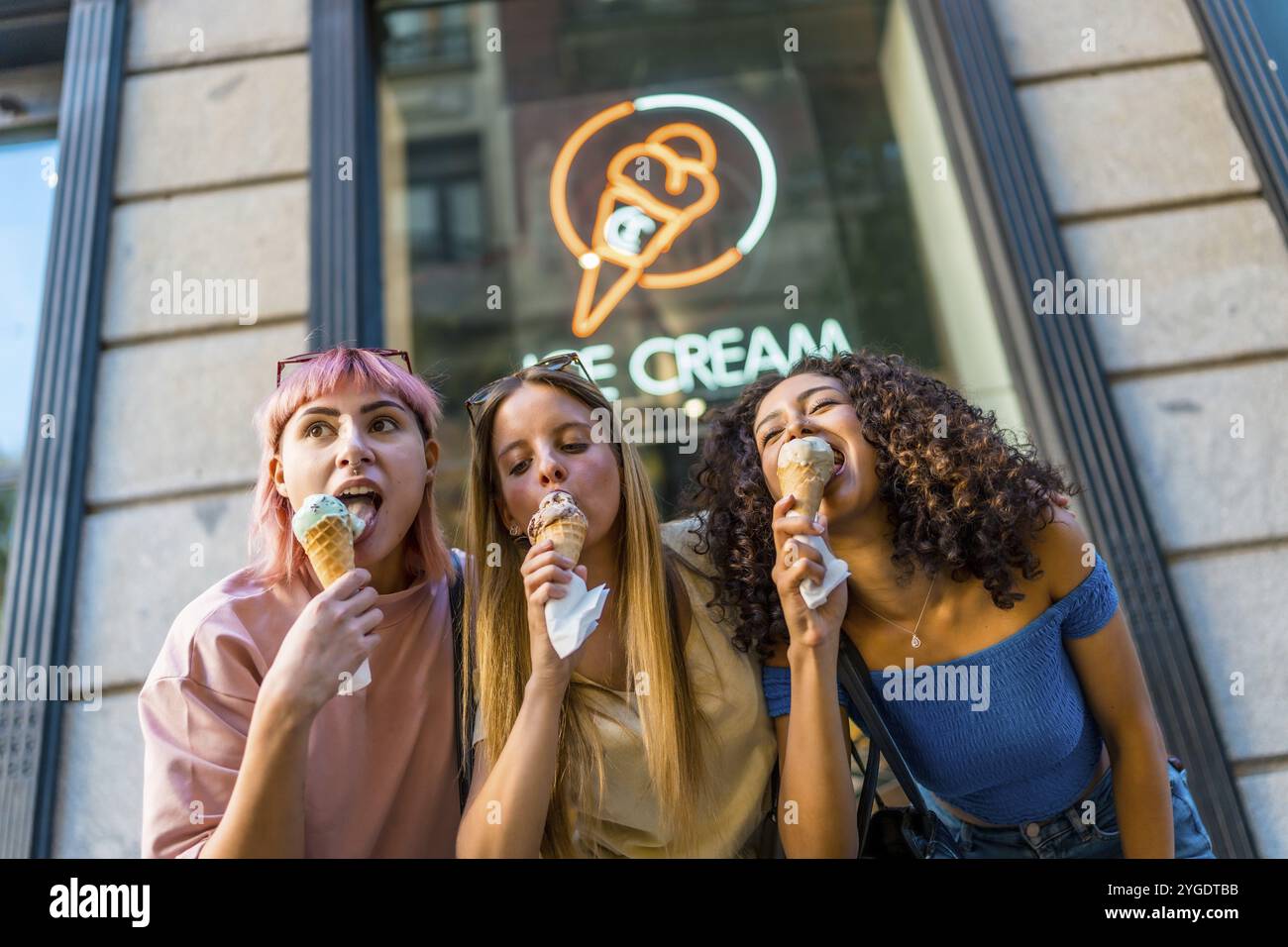 Foto con vista dall'angolo basso di tre diverse amiche che si godono un delizioso gelato fuori dal negozio Foto Stock