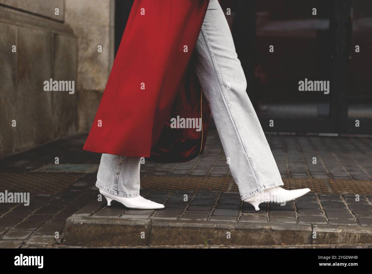 Primi piani di una donna elegante e irriconoscibile che cammina per strada urbana, indossa jeans, cappotto Bordeaux e décolleté con tacco bianco alla moda, catturando il cit Foto Stock