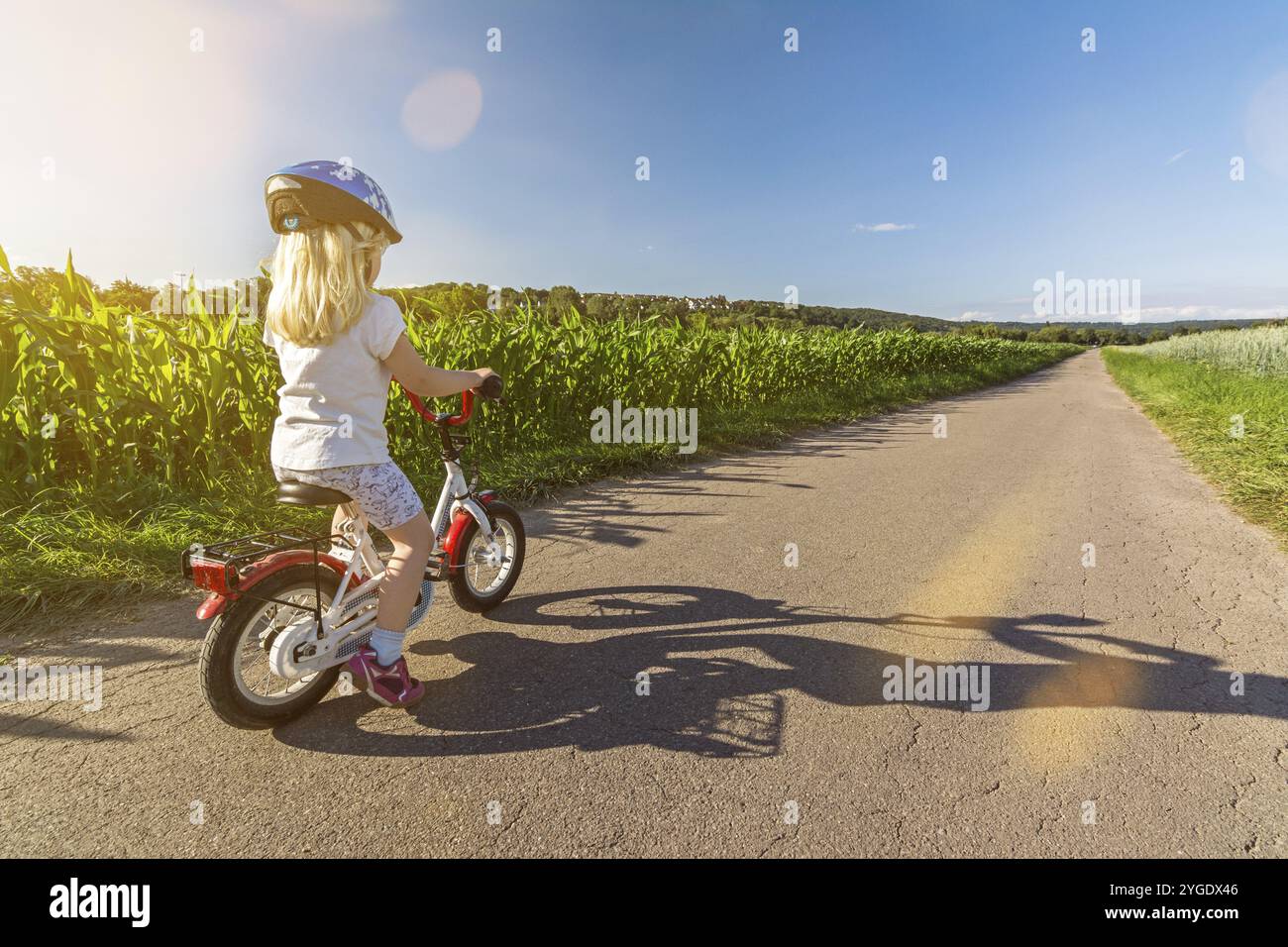 Giovane bionda sulla sua piccola bicicletta su una strada in paesaggio rurale in una giornata di sole in primavera Foto Stock