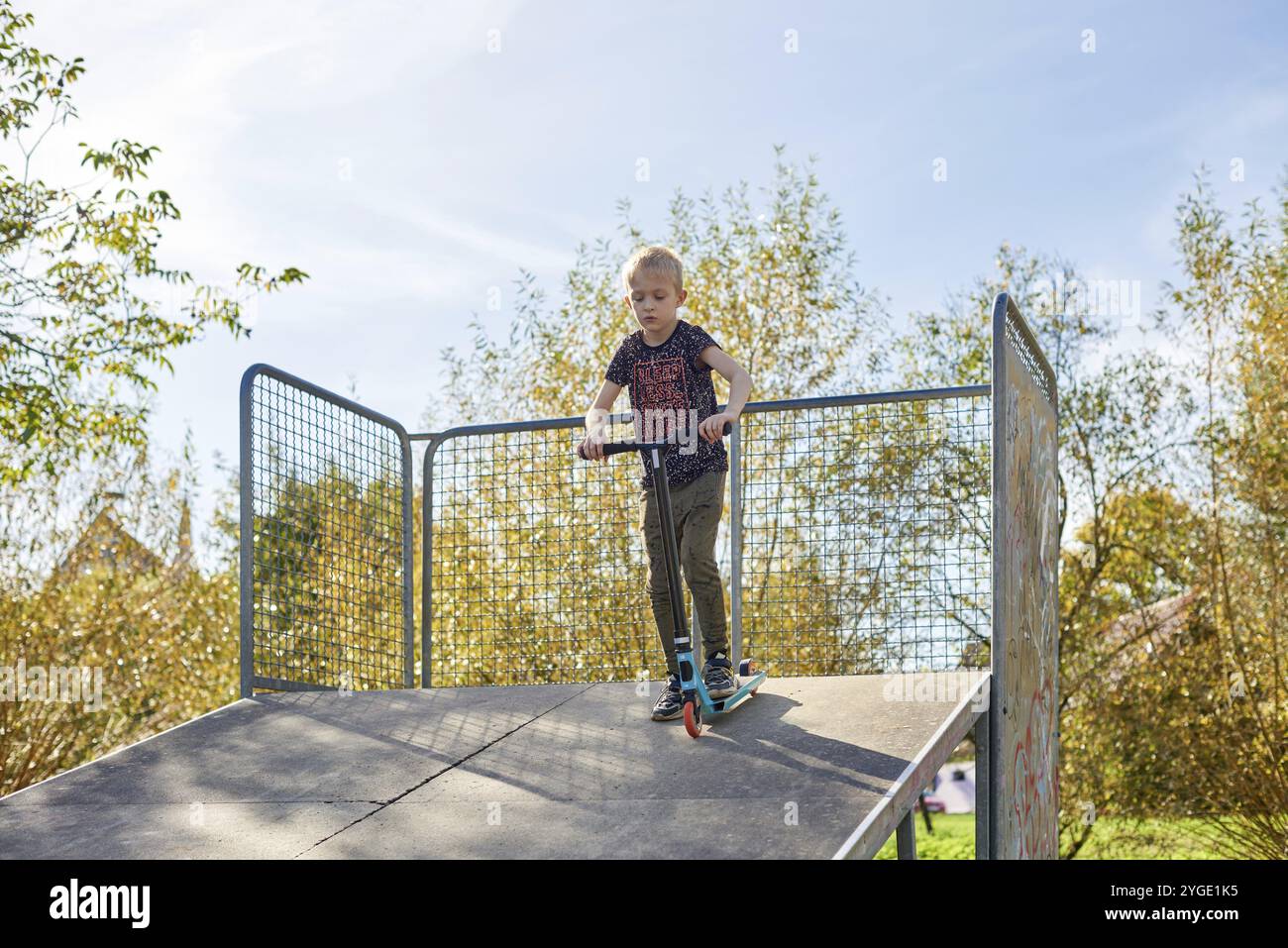 Bambino su kick scooter nel parco. I ragazzi imparano a rullo di skate board. Little Boy pattinaggio sulla soleggiata giornata estiva. Attività all'aperto per i bambini sulla sicurezza residen Foto Stock