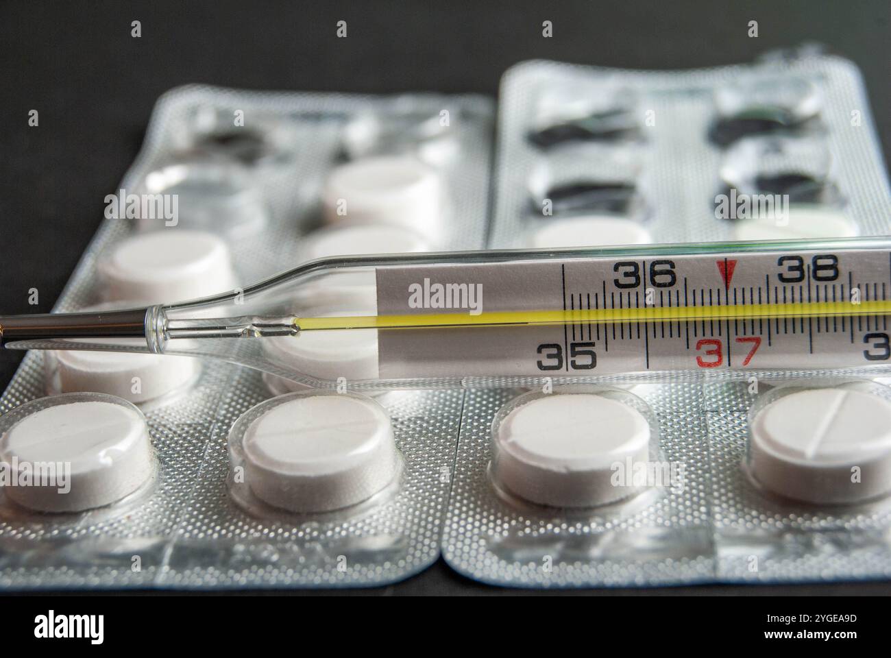 Immagine dettagliata delle pillole di paracetamolo con un termometro, enfatizzando la salute e il trattamento del raffreddore / influenza, impostato su uno sfondo scuro e contrastante. Foto Stock