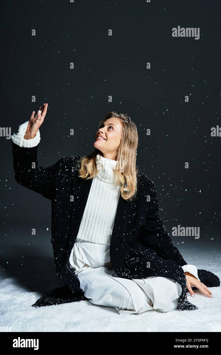 Una bella donna gode di un momento sereno mentre è circondata da dolci fiocchi di neve al coperto. Foto Stock