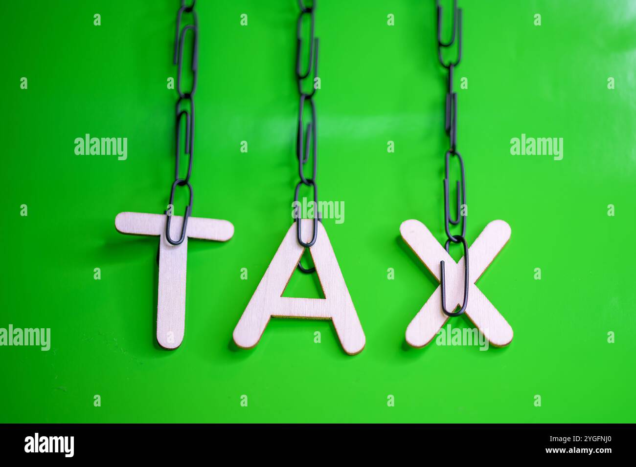 Lettere di legno che scrivono la parola "TASSA" appesa su graffette nere su sfondo verde Foto Stock
