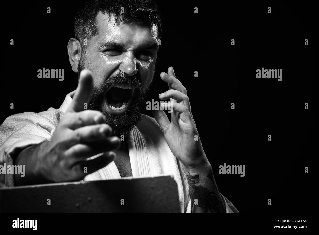 Ritratto di un bell'uomo di karate che rompe mattoni di cemento. Il combattente di karate arrabbiato rompe la lastra di cemento con la mano. Forte maestro di karate muscoloso Foto Stock