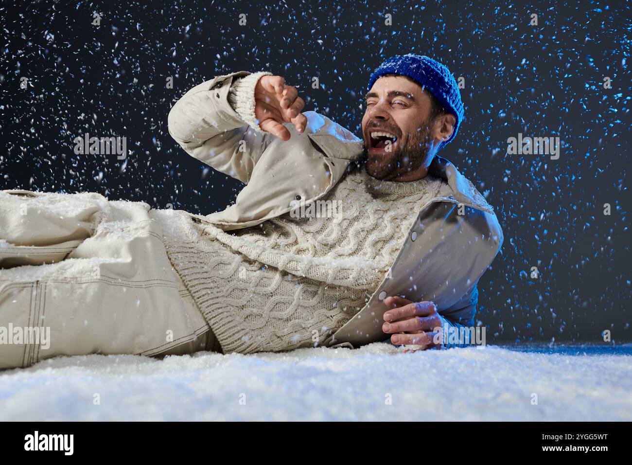 Un giovane ride mentre sdraiato sulla neve, abbracciando la gioia dell'inverno in un'atmosfera giocosa. Foto Stock