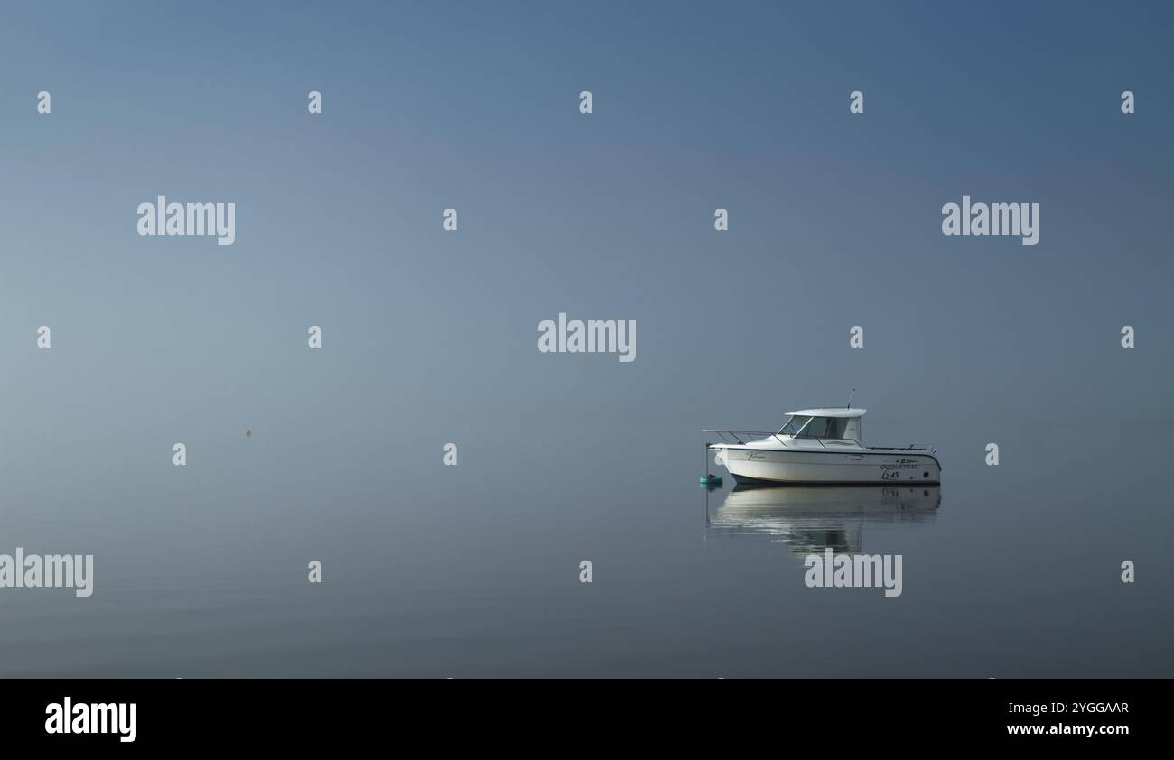 Il motoscafo Ocqueteau è ormeggiato su Una boa in Un calmo nebbioso, giornata di caccia con acqua ferma e senza vento, Christchurch Harbour, Regno Unito Foto Stock