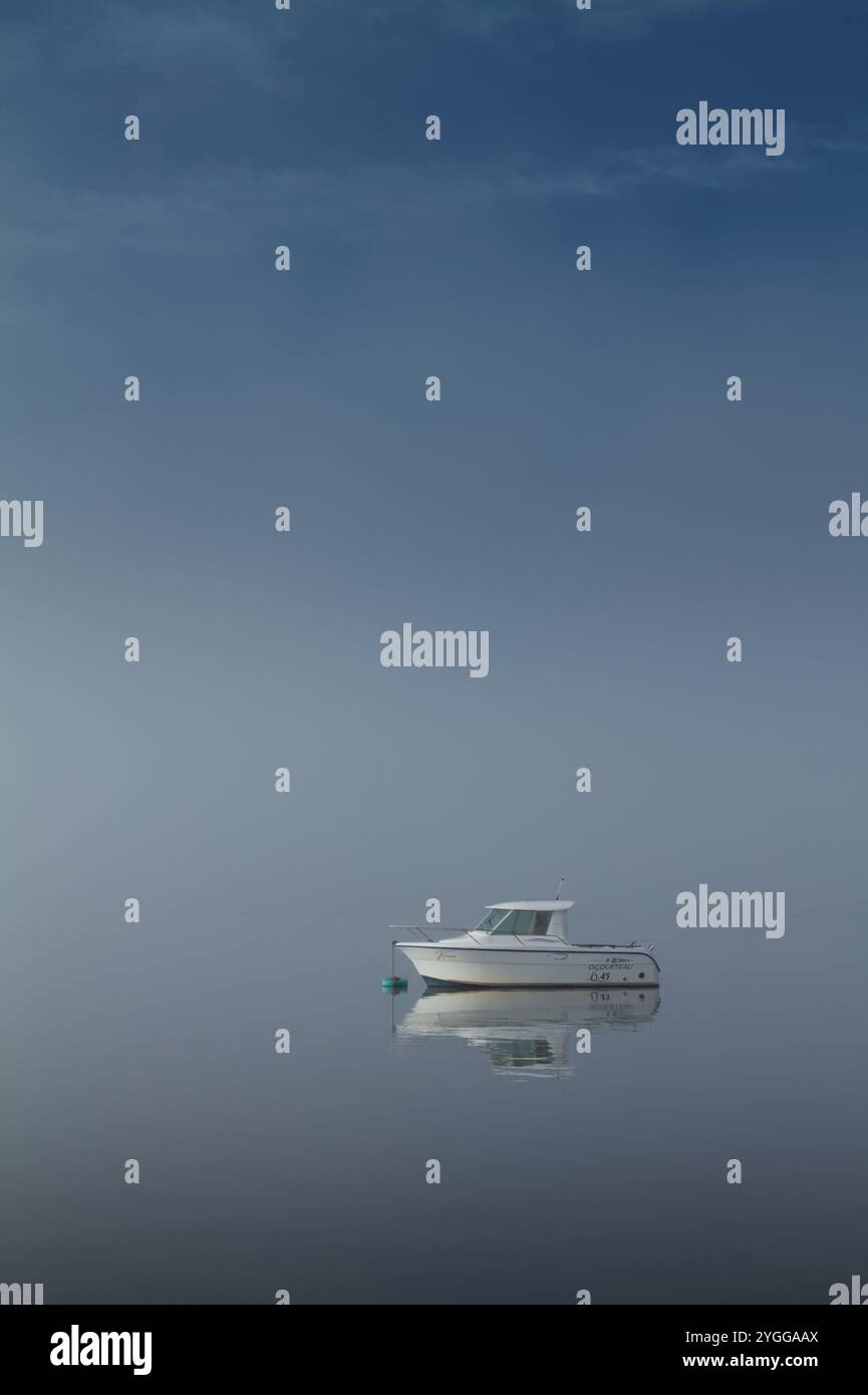 Il motoscafo Ocqueteau è ormeggiato su Una boa in Un calmo nebbioso, giornata di caccia con acqua ferma e senza vento, Christchurch Harbour, Regno Unito Foto Stock