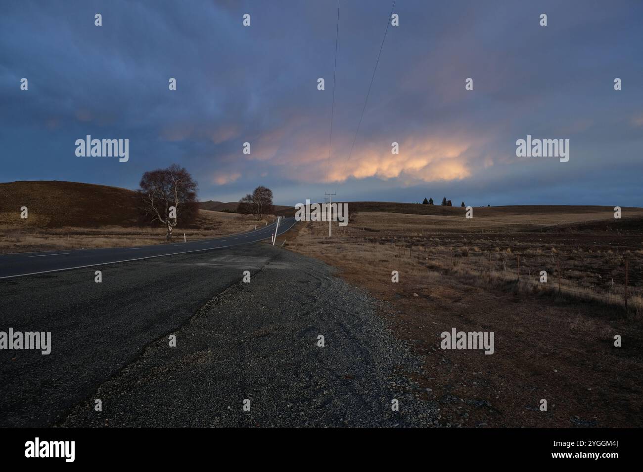 Strada sterrata nel paesaggio di tussock verso il cielo nuvoloso alla fine del tramonto, South Island, nuova Zelanda Foto Stock