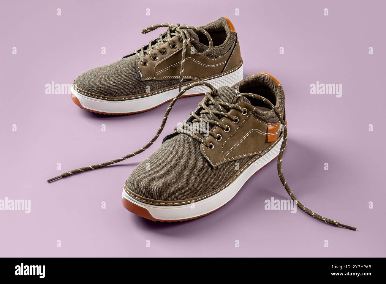 Un paio di scarpe in tela cachi su sfondo viola pallido. Nuove scarpe in tessuto marrone con suola bianca e allacciatura. Scarpe per camminare e correre. Foto Stock