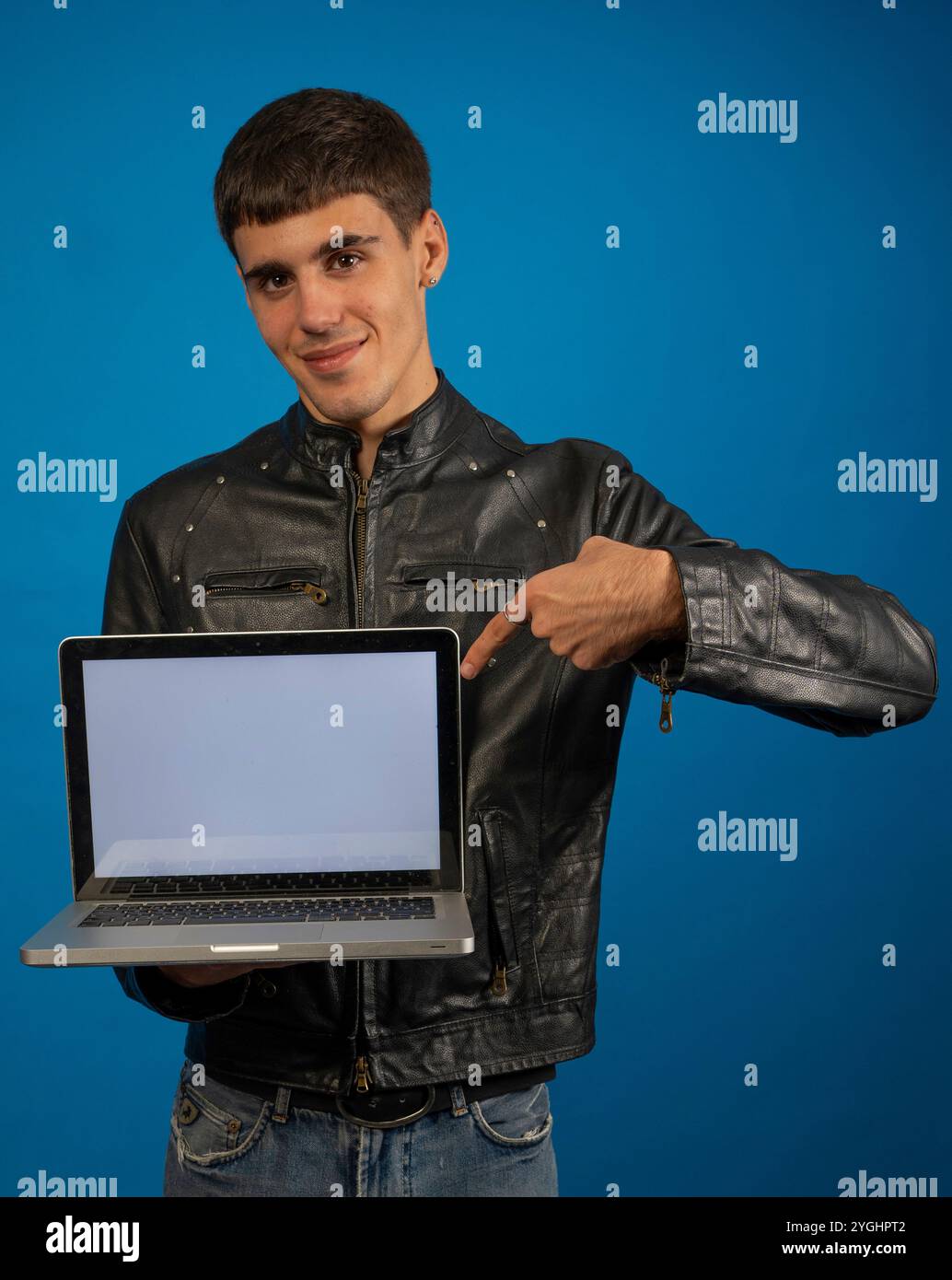 Giovane programmatore che punta al suo laptop con schermo vuoto, isolato su sfondo blu Foto Stock