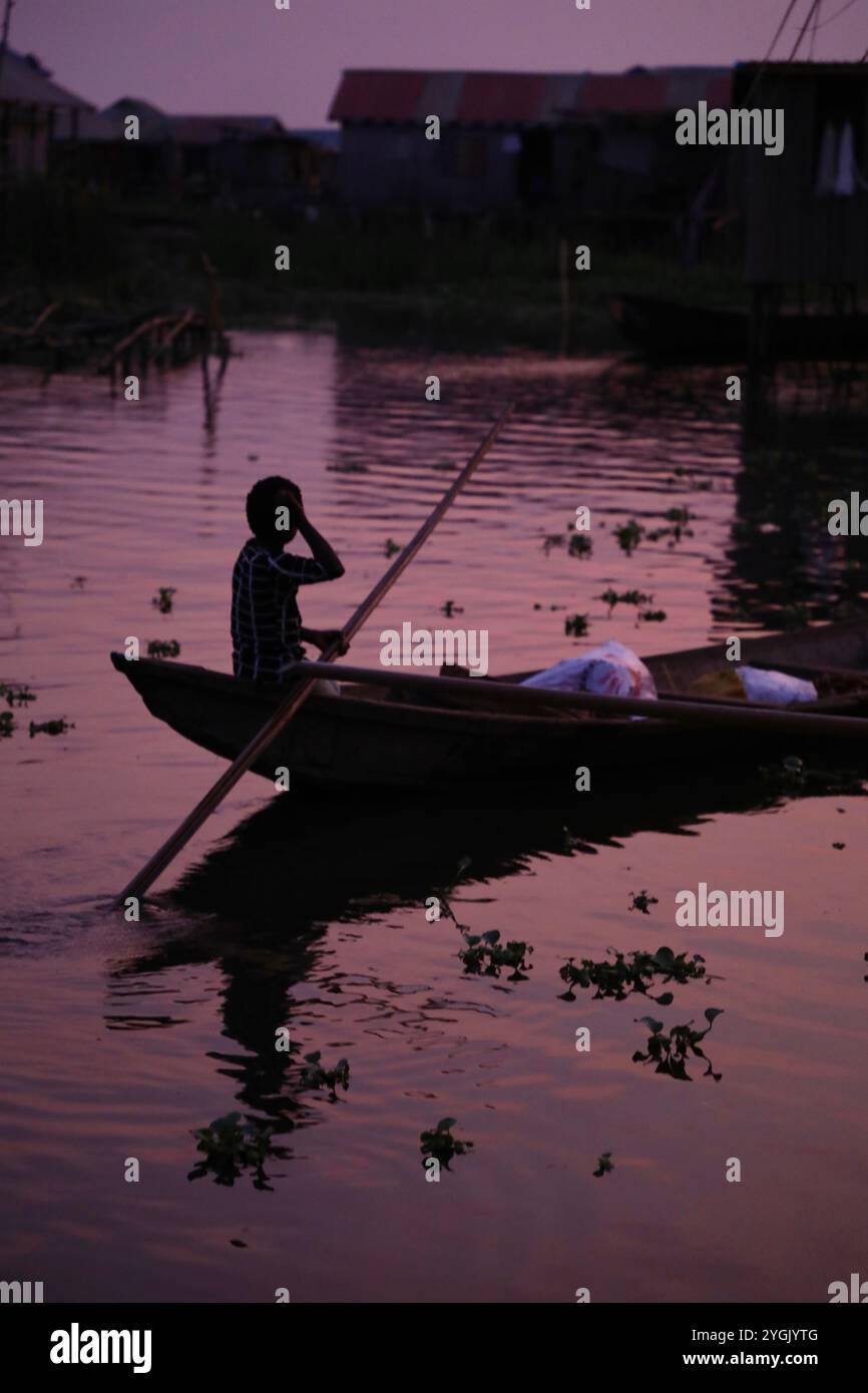 Un abitante del villaggio lacustre di Ganvié nel Benin viaggia in piroga al tramonto. Non ci sono strade a Ganvié, quindi gli abitanti si aggirano solo facendo piroghe. Conosciuto come la Venezia dell'Africa, il lago Nokoué è costruito quasi interamente su palafitte. I primi abitanti del lago si stabilirono qui nel XVIII secolo per sfuggire alle incursioni degli schiavi. Oggi, decine di migliaia di persone vivono sul lago, e la loro attività principale è la pesca. Foto Stock