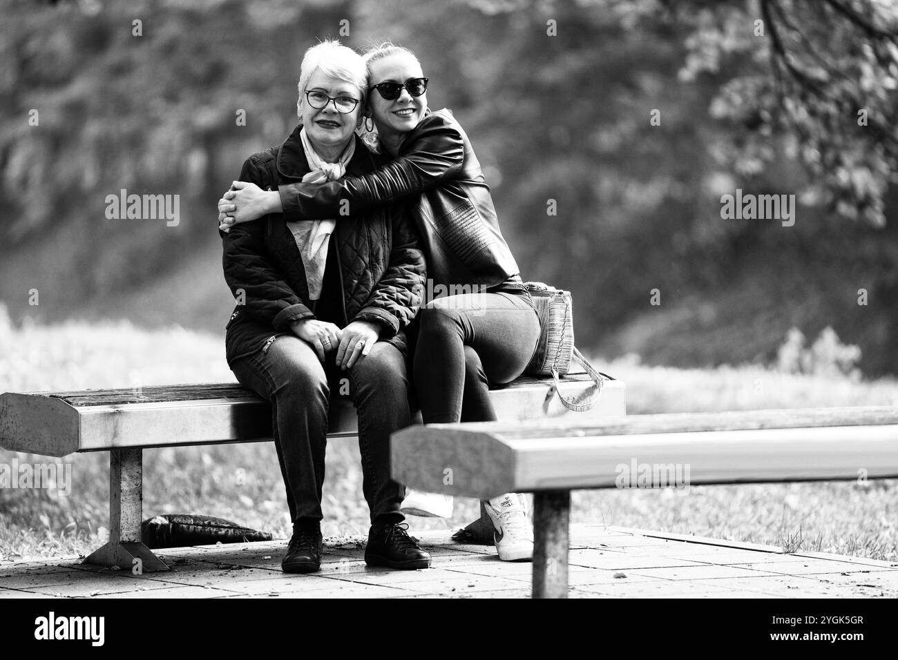 Un'anziana dai capelli grigi e sua figlia si rilassano in un parco, godendosi il sole autunnale. Riflettono la loro giornata informale e accogliente Foto Stock