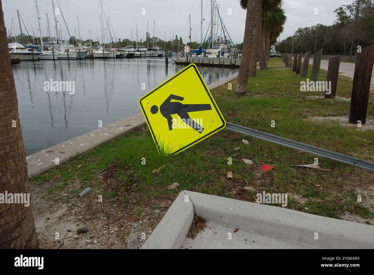 Curva a S di Seawall sulla destra con palme verdi. Soffiato sopra il cartello giallo riflettente per pedoni Crossing Road, lato destro del lungomare. Vista I. Foto Stock