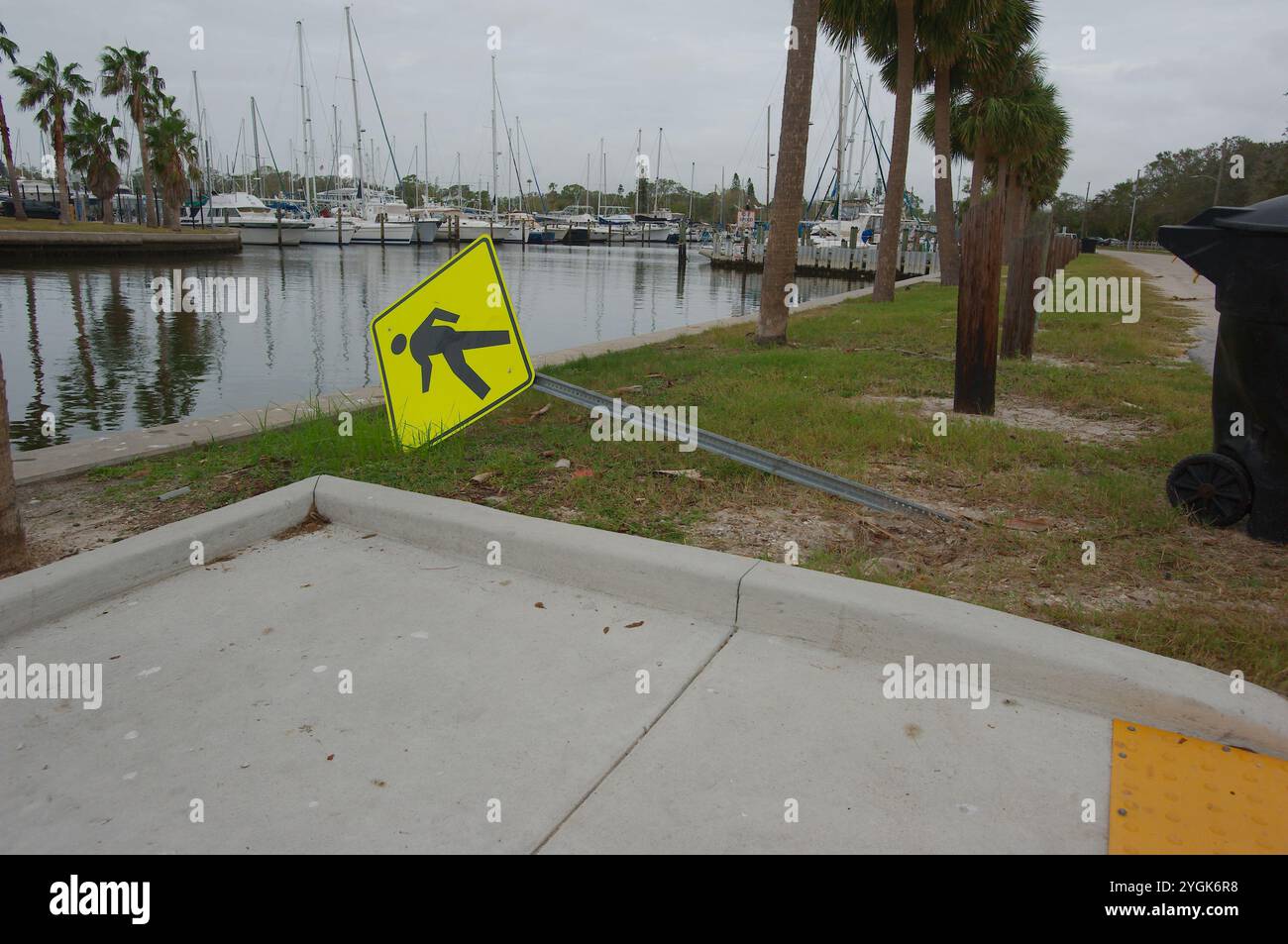 Curva a S di Seawall sulla destra con palme verdi. Soffiato sopra il cartello giallo riflettente per pedoni Crossing Road, lato destro del lungomare. Vista I. Foto Stock