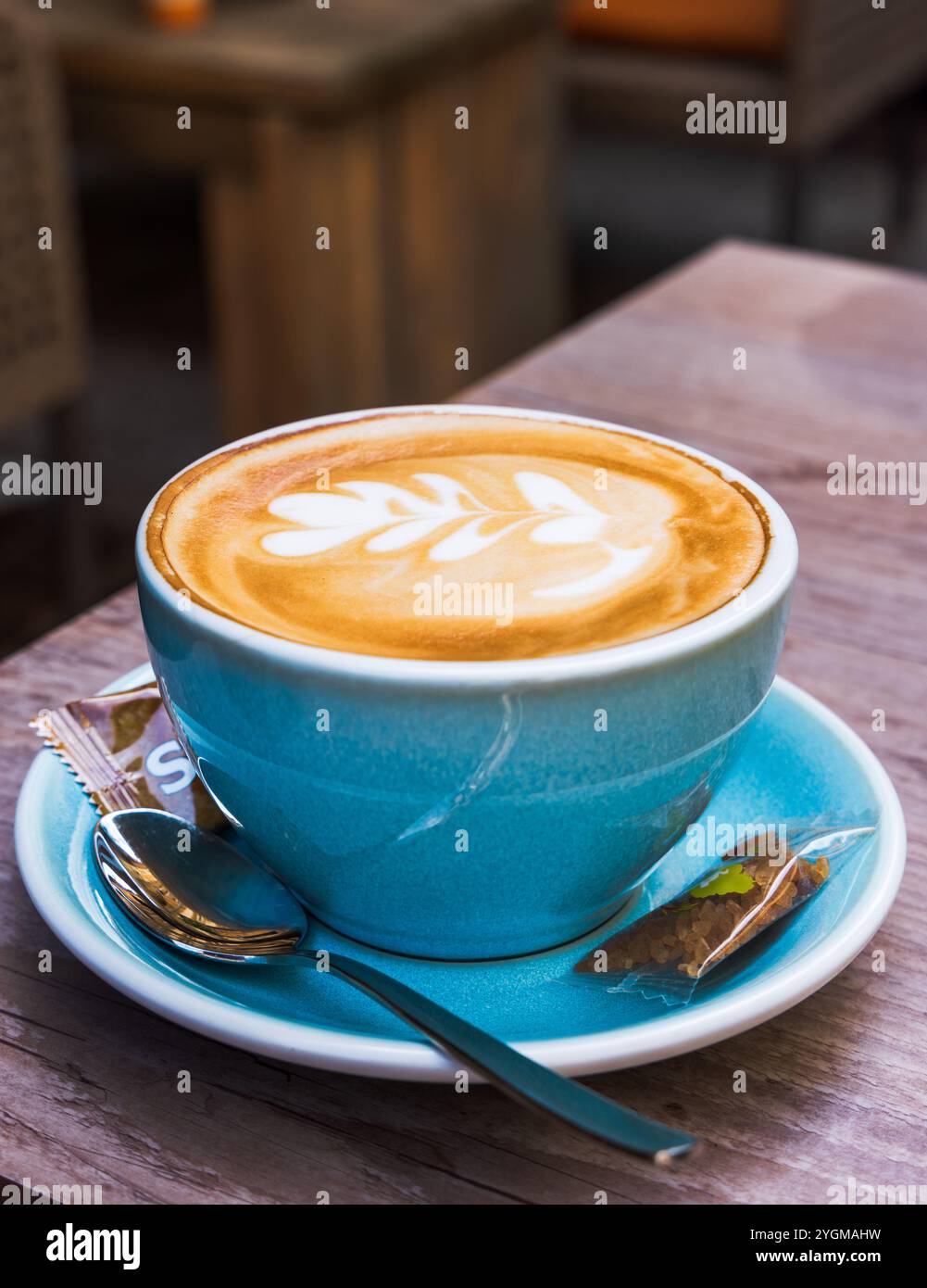 Un cappuccino caldo fresco in una tazza blu con un fiore sulla parte superiore Foto Stock