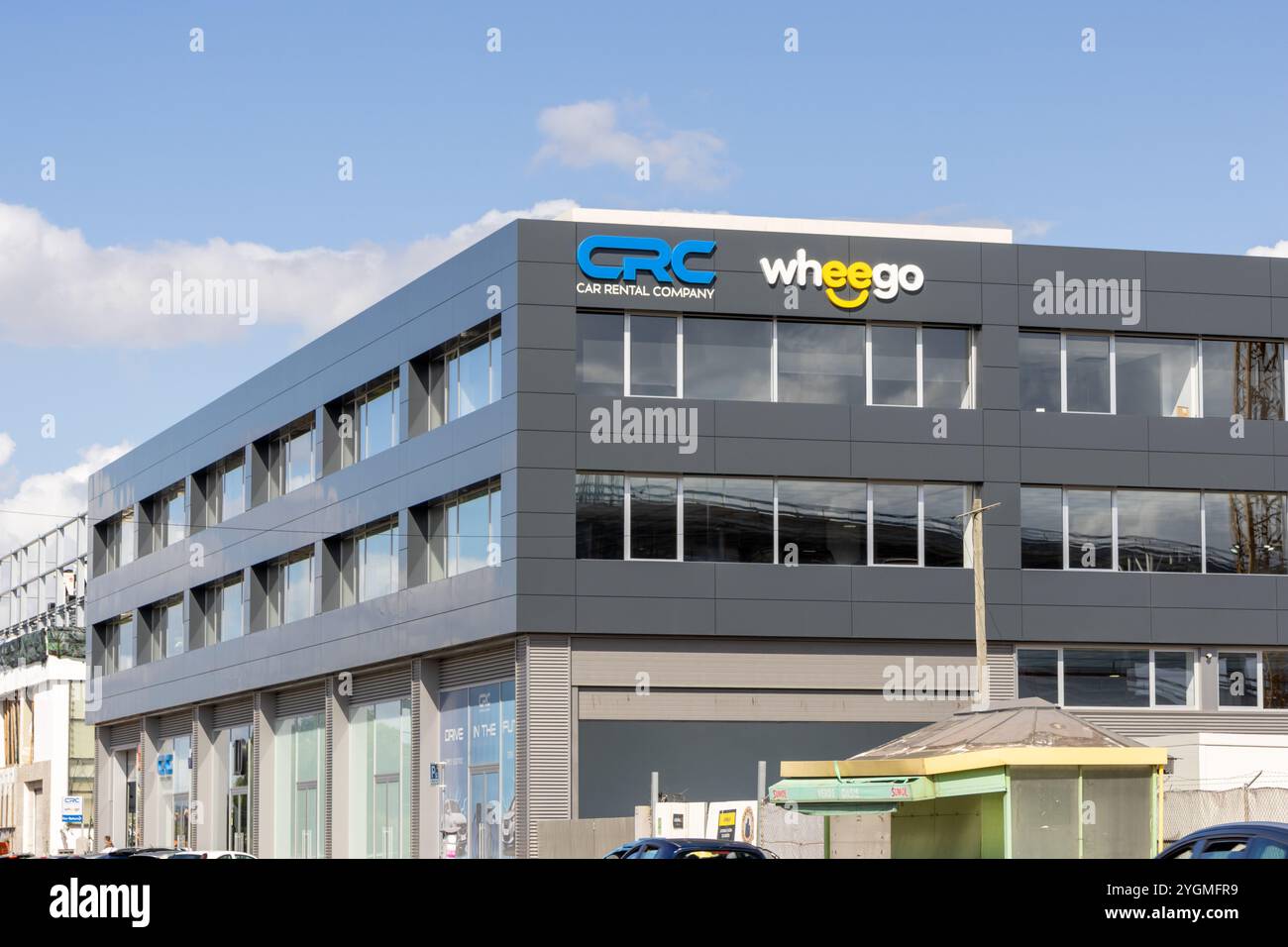 Edificio moderno che mostra i loghi delle società di autonoleggio wheego e crc contro un cielo blu, suggerendo una fiorente attività di autonoleggio Foto Stock