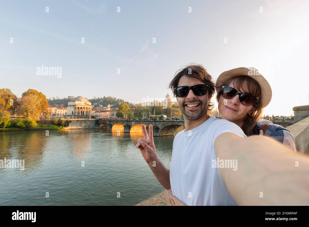 Felice coppia sorridente che scatta un selfie di fronte al paesaggio urbano di Torino (Torino) al tramonto con i dettagli della Gran madre. Uno dei più importanti Foto Stock
