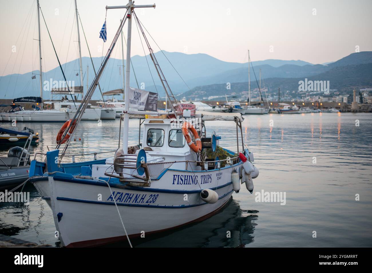 Una vista pittoresca di una baia costiera con barche a Hersonissos, Creta. Le acque tranquille incontrano l'affascinante cittadina, incorniciata dalla bellezza naturale dell'isola. Foto Stock