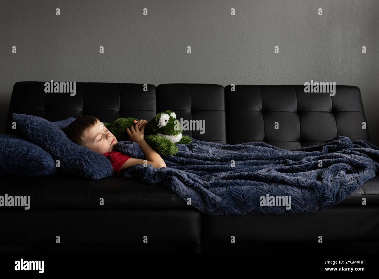 Bambino che dorme sul divano con peluche sotto una coperta blu Foto Stock