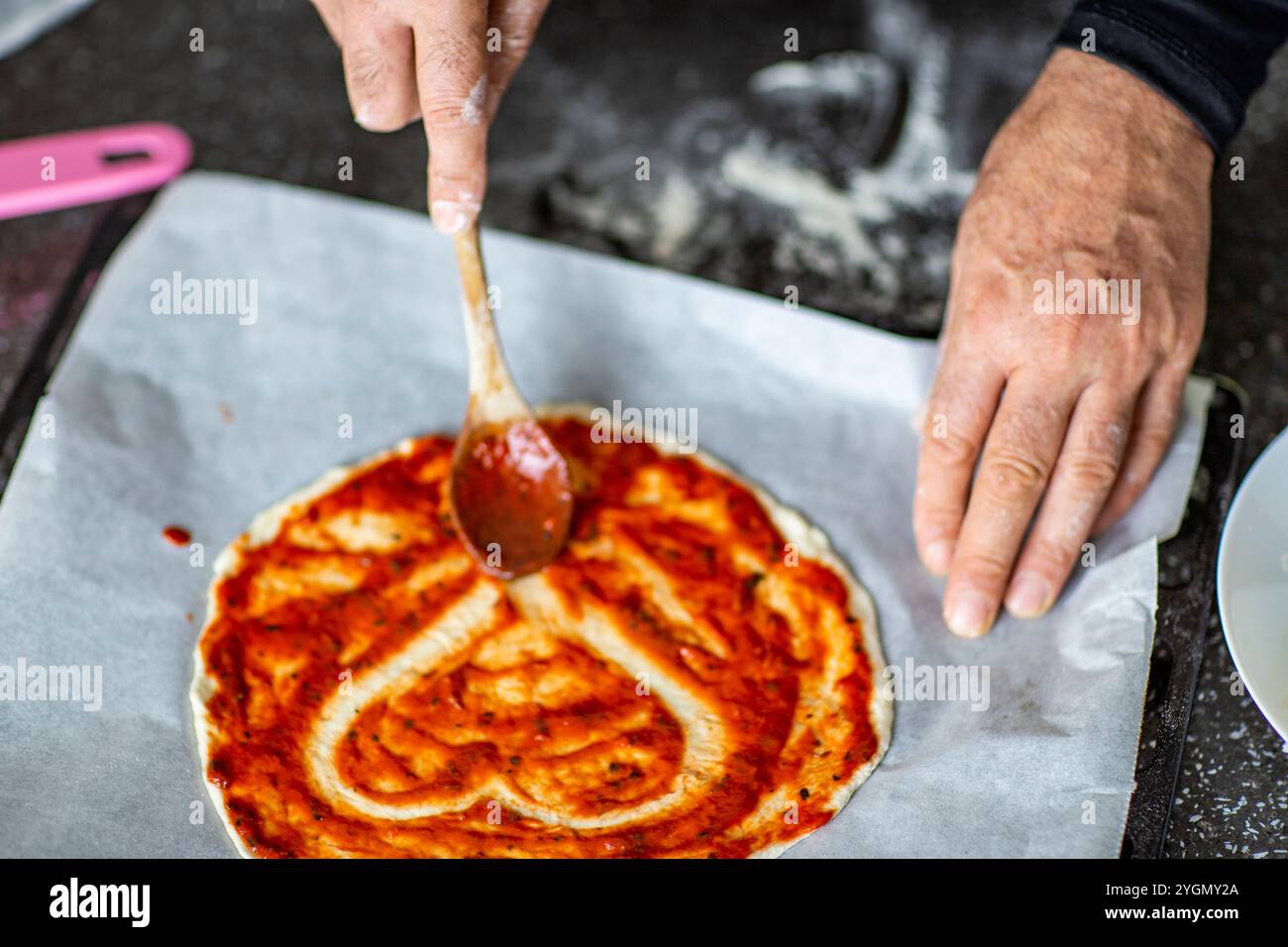 Persona che aggiunge salsa di pomodoro alla pizza a forma di cuore Foto Stock