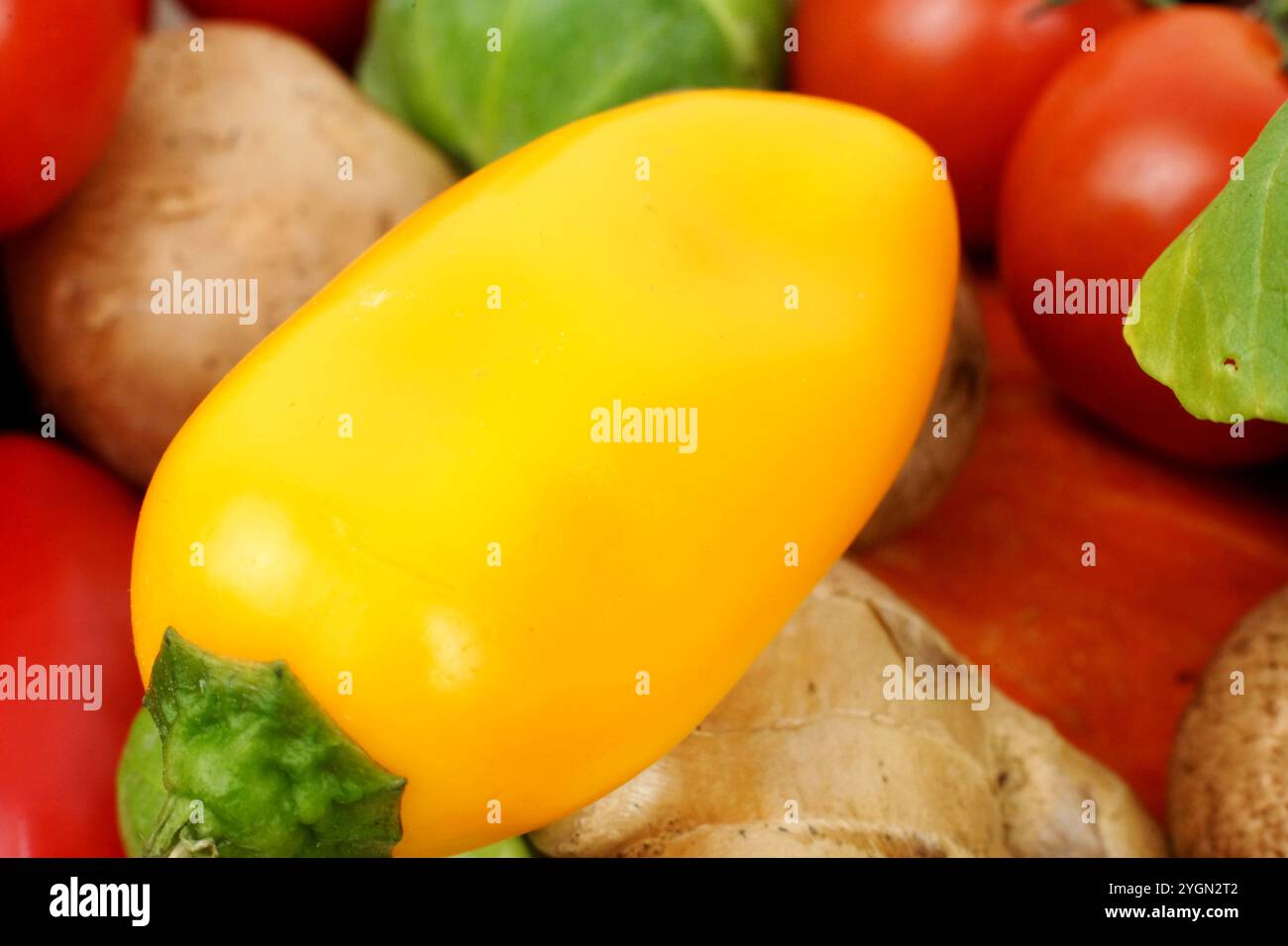 Primo piano di un peperoncino giallo con profondità di campo bassa. Lo sfondo mostra altre verdure e zenzero. Il colore dominante è giallo, con beige Foto Stock