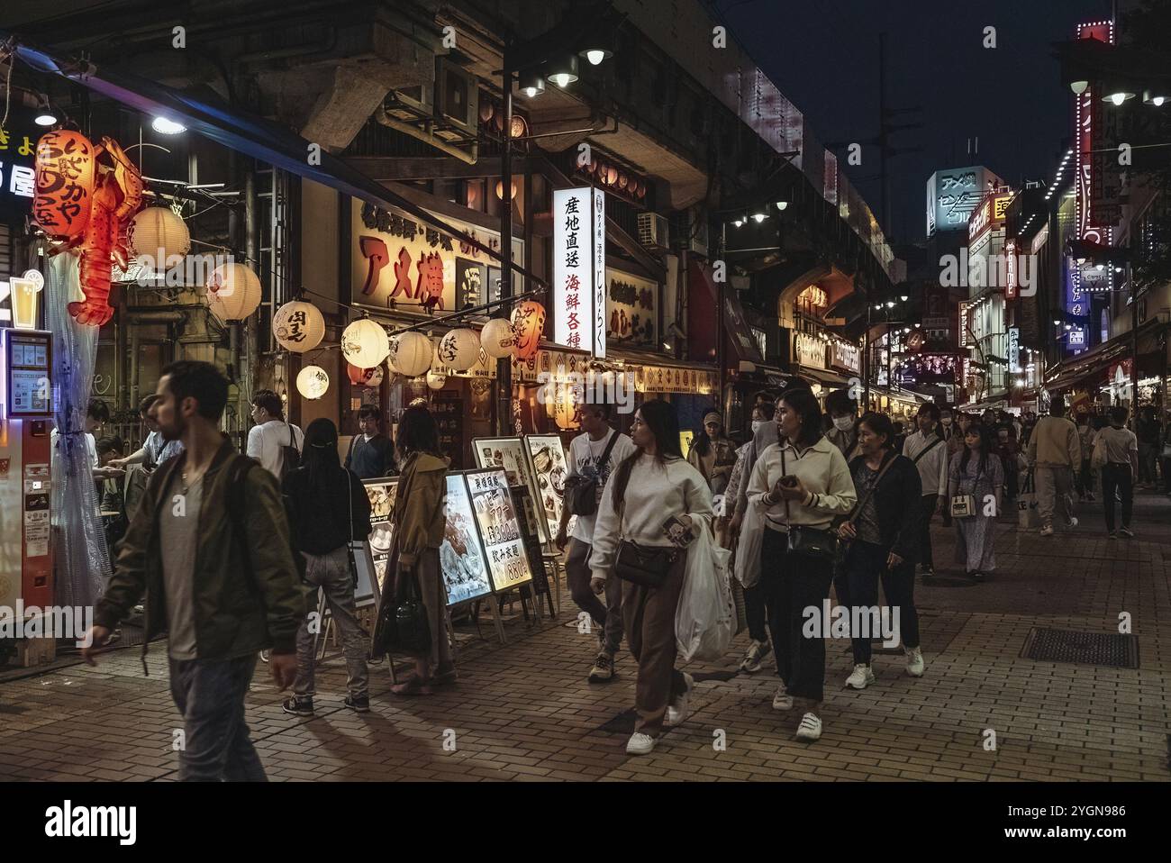 I turisti passano davanti ai ristoranti in serata sulla strada dello shopping Ameyoko nel quartiere Ueno nel quartiere Taito di Tokyo in Giappone Foto Stock