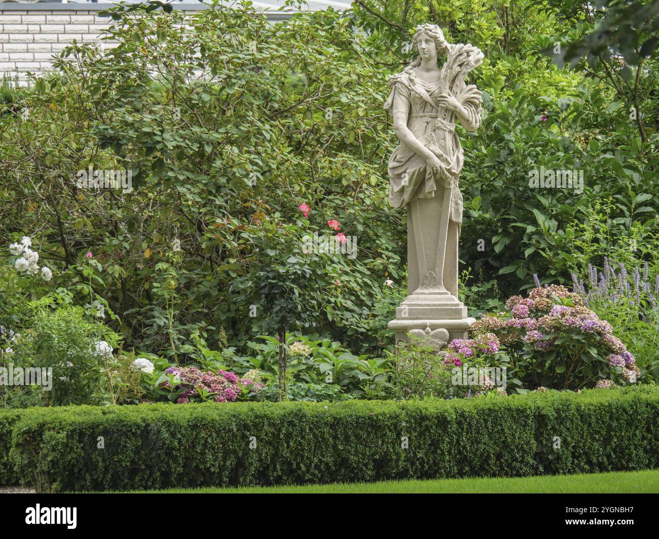 Una statua incorniciata da fiori colorati in un giardino lussureggiante, Borken, Renania settentrionale-Vestfalia, Germania, Europa Foto Stock