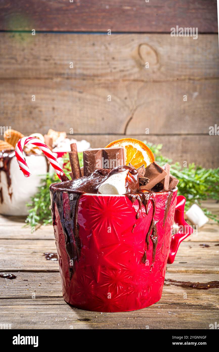 Tazze di cioccolato caldo in stile natalizio con vari condimenti: Fette di cioccolato, spezie, dolci, biscotti, caramelle e pani di zenzero, accogliente in legno Foto Stock