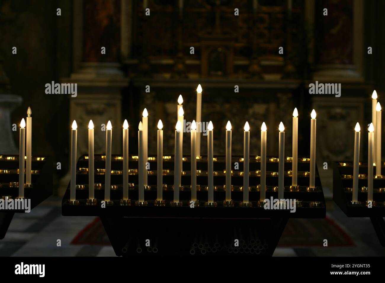 Molte piccole candele elettriche che bruciano sui portacandele in legno illuminano l'interno di una chiesa Foto Stock