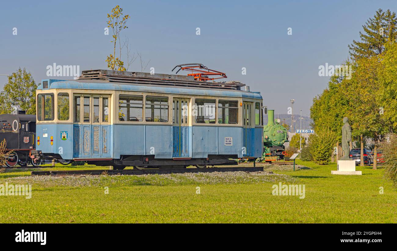 Slavonski Brod, Croazia - 22 ottobre 2024: Vecchio tram elettrico trasporto pubblico e locomotiva a vapore presso il Parco industriale Turistico Djuro Djakovic all'aperto Foto Stock