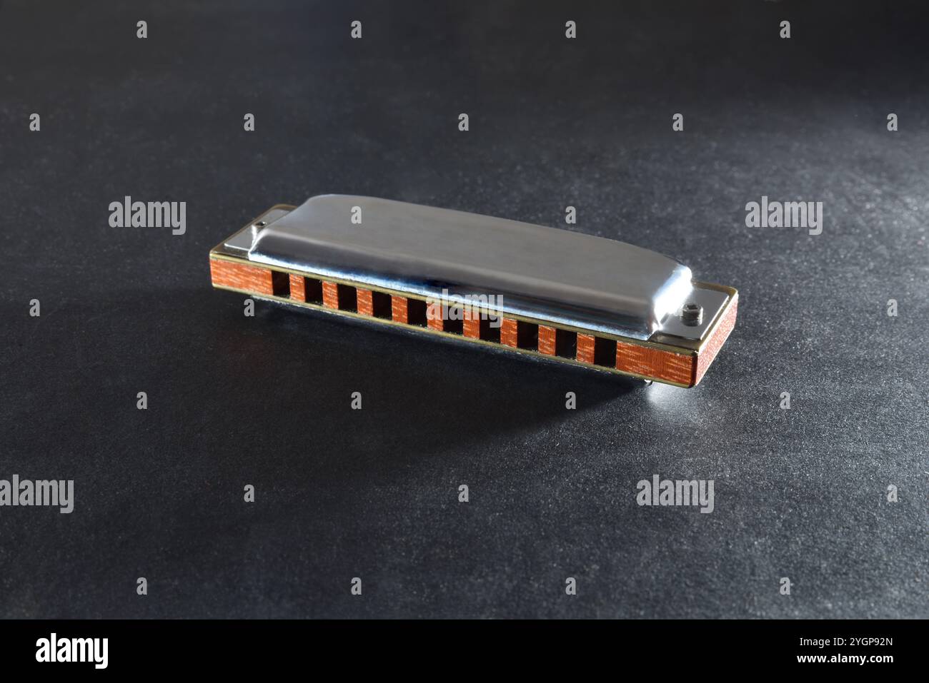 armonica in metallo e legno con una striscia di fori appoggiata su una base con trama scura. Vista dall'alto in alto. Foto Stock