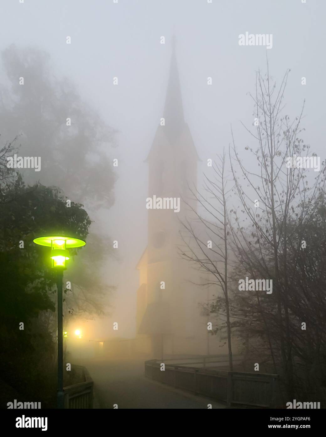 Chiesa in fitta nebbia con lanterna verde. La chiesa di derivazione di Guggenthal, nella nebbia di una sera di novembre. Chiesa cattolica romana dedicata alla Santa Croce. Foto Stock