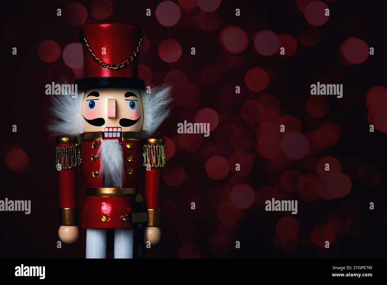 Primo piano del soldato natalizio dello schiaccianoci in legno con luci natalizie e spazio per testo su sfondo rosso. Sfondo del concept natalizio Foto Stock