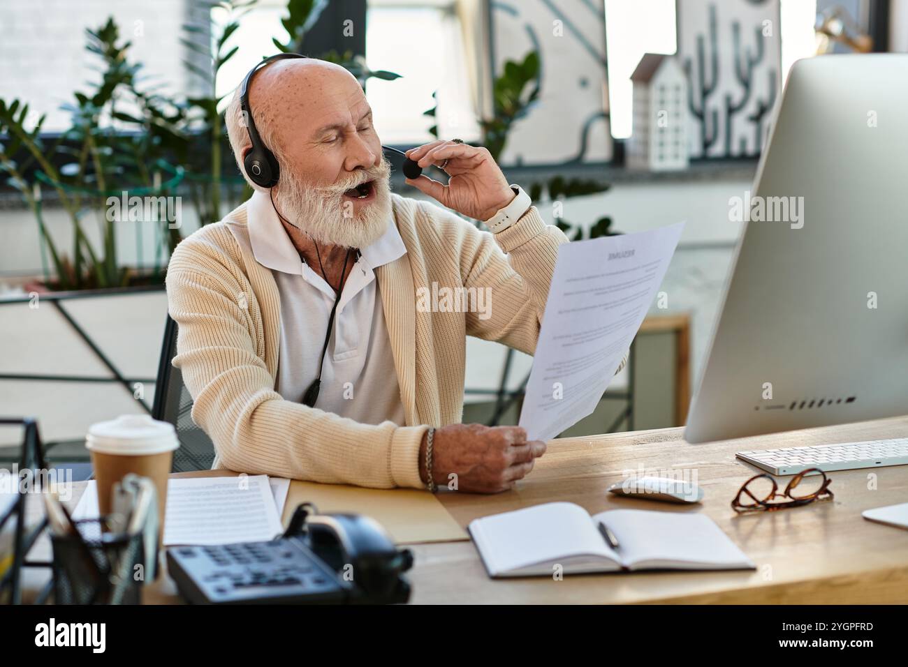Un uomo d'affari anziano in un elegante abbigliamento casual conduce una chiamata al cliente, immerso nel lavoro all'interno di un ufficio elegante. Foto Stock