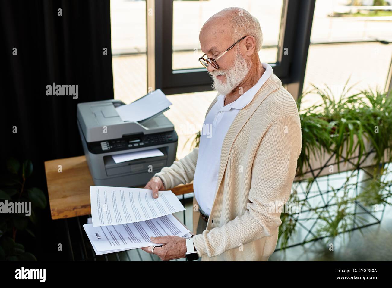 Un elegante senior manager controlla i documenti importanti mentre è circondato dal verde in uno spazio di lavoro moderno. Foto Stock